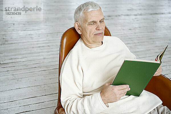 Mann liest ein Buch und sitzt zu Hause auf einem Stuhl