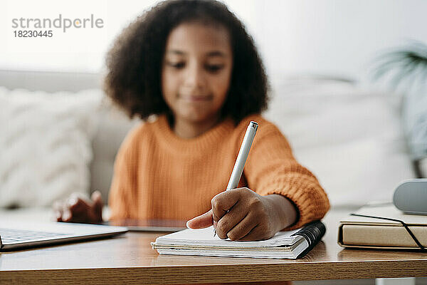 Mädchen mit Stift und Notizblock macht zu Hause Hausaufgaben