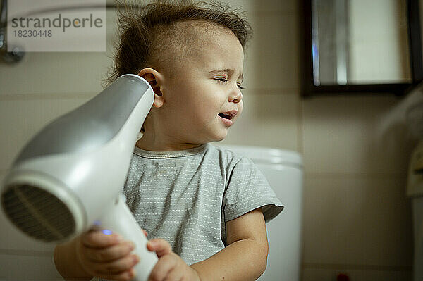 Boy with eyes closed blowing hair with dryer at home