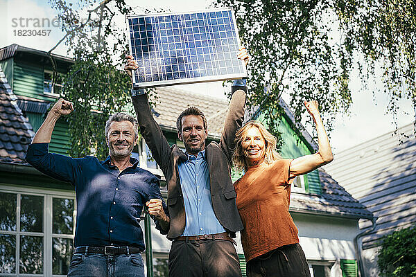 Glückliche Männer und Frauen  die ihre Muskeln spielen lassen  während ein Immobilienmakler Solarpanel durch Sonnenlicht auflädt