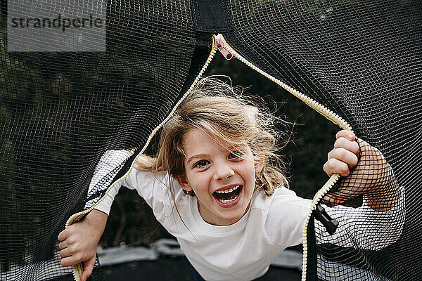 Glückliches Mädchen  das durch das Netz auf dem Trampolin im Garten schaut