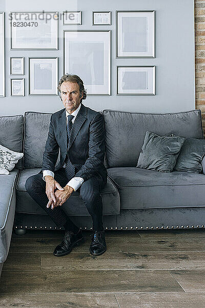 Selbstbewusster reifer Geschäftsmann im Anzug sitzt zu Hause auf dem Sofa