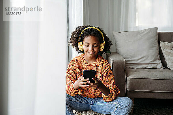 Lächelndes Mädchen mit kabellosen Kopfhörern und Smartphone zu Hause