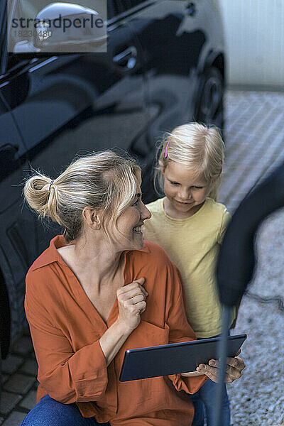 Glückliche Mutter zeigt ihrer Tochter im Vorgarten einen Tablet-PC