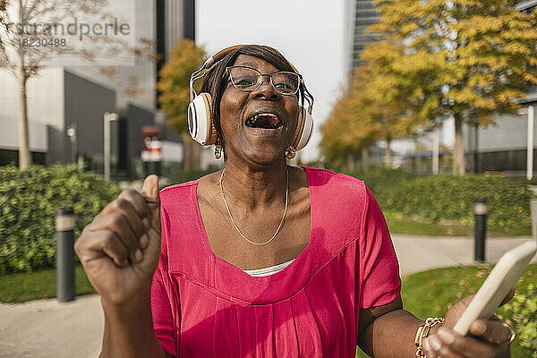 Glückliche Frau mit kabellosen Kopfhörern genießt den Park