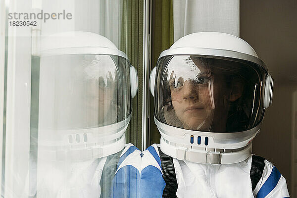 Nachdenkliches Mädchen im Weltraumkostüm  das zu Hause durch das Fenster schaut