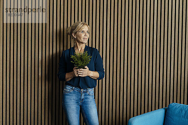 Geschäftsfrau mit Topfpflanze vor der Wand im Büro