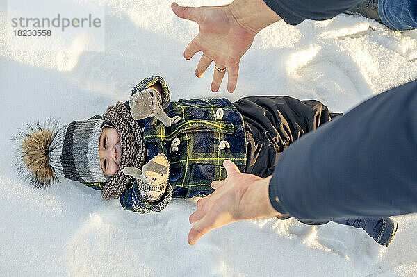 Hands of man reaching for baby boy lying on snow