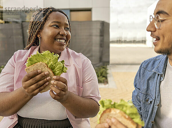 Glückliches junges Paar mit Sandwich  das am Fußweg steht