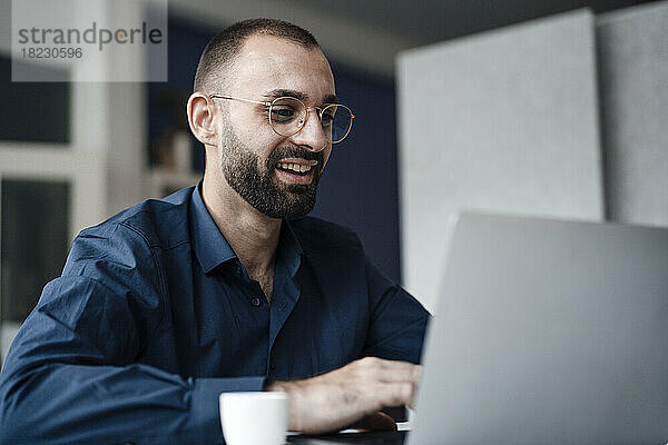 Happy businessman using laptop at desk in office