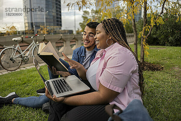 Glückliches junges Paar liest gemeinsam ein Buch auf Gras