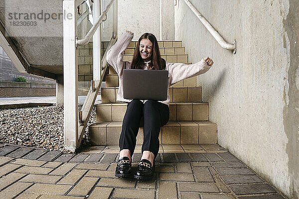 Glückliche junge Frau mit Laptop auf der Treppe