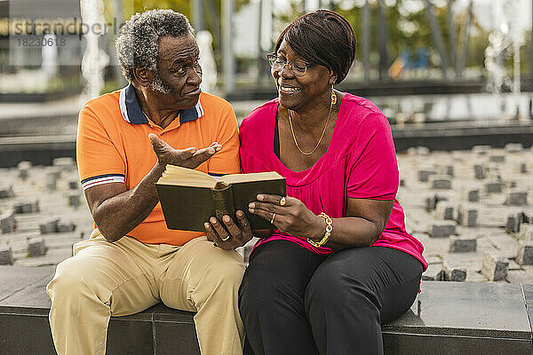 Älterer Mann spricht mit Frau  die ein Buch liest  das an der Wand sitzt