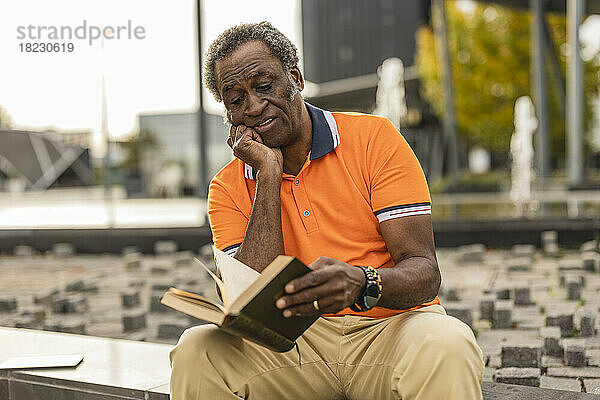 Älterer Mann mit der Hand am Kinn  der ein Buch liest