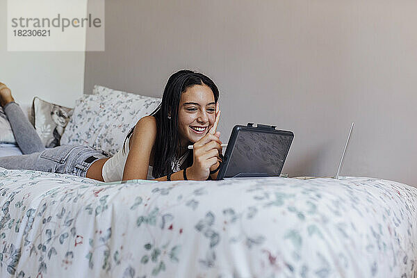 Glückliches Mädchen mit Tablet-PC  das zu Hause im Bett liegt