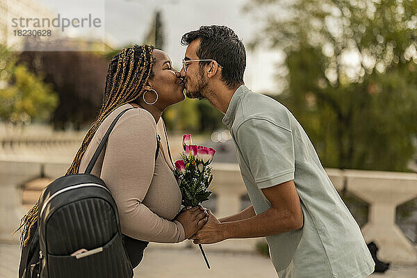 Junges Paar küsst sich mit Blumenstrauß am Fußweg