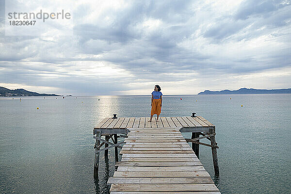 Woman standing on jetty amidst sea under cloudy sky