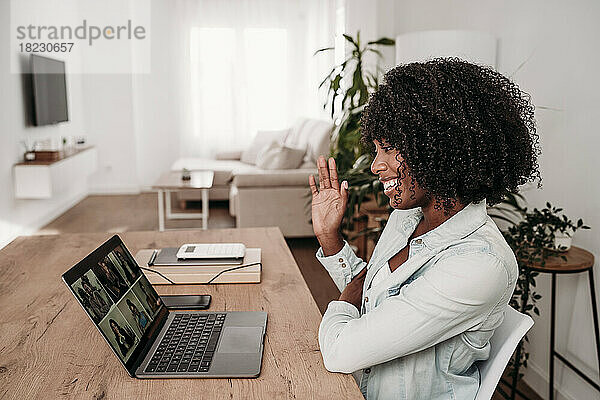 Lächelnde Geschäftsfrau winkt bei Videoanruf über Laptop im Heimbüro
