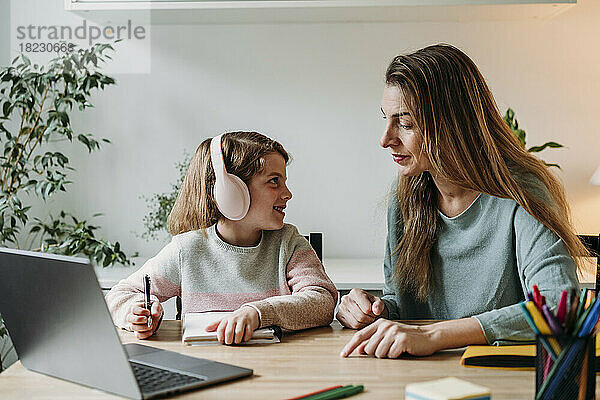 Mutter hilft Mädchen im Studium  das zu Hause mit Laptop auf dem Tisch sitzt