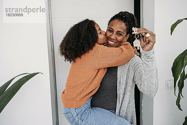 Glückliches Mädchen umarmt Mutter und hält Schlüssel für neues Haus