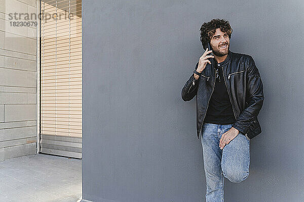 Lächelnder Mann  der vor einer grauen Wand mit dem Mobiltelefon spricht