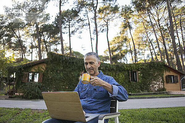 Reifer Mann trinkt Kaffee und benutzt Laptop im Freien