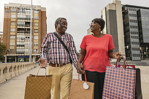 Glückliches älteres Paar  das mit Einkaufstüten auf dem Fußweg läuft