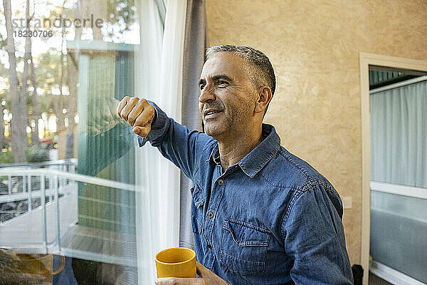 Reifer Mann hält Kaffeetasse zu Hause und schaut aus dem Fenster