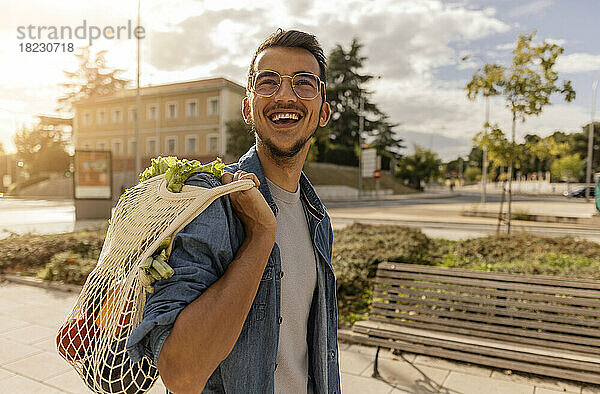 Glücklicher junger Mann mit einer Tüte Gemüse steht am Fußweg