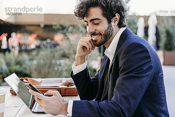Lächelnder Geschäftsmann mit der Hand am Kinn und Smartphone