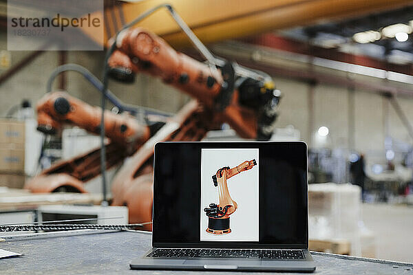Laptop mit Roboterarmfoto am Schreibtisch in der Industrie