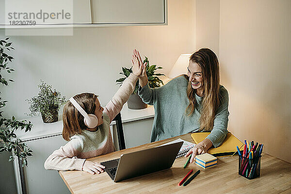 Glückliche Mutter gibt ihrer Tochter High-Five  die mit Laptop am Tisch sitzt