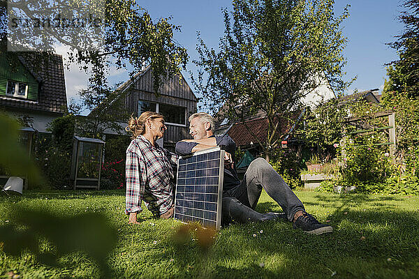 Älteres Paar sitzt mit Solarpanel auf Gras im Hinterhof