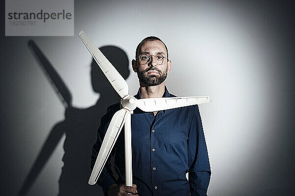 Businessman holding model of wind turbine in front of gray wall