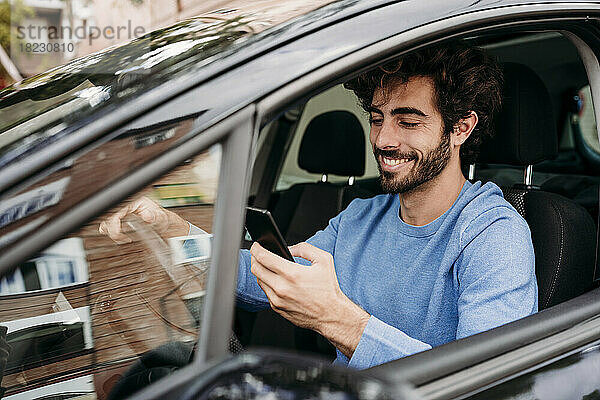 Lächelnder Mann benutzt Smartphone im Auto