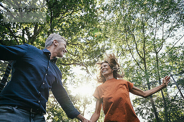 Cheerful mature man and woman enjoying under tree on sunny day
