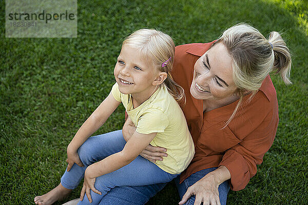 Lächelnde Mutter mit Tochter  die auf Gras sitzt