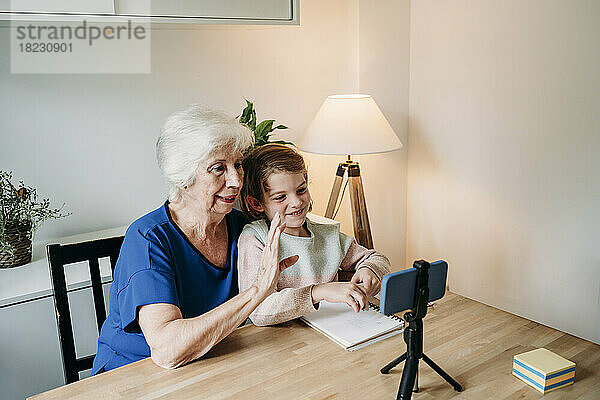 Ältere Frau mit lächelnder Enkelin  die zu Hause einen Videoanruf auf dem Mobiltelefon führt