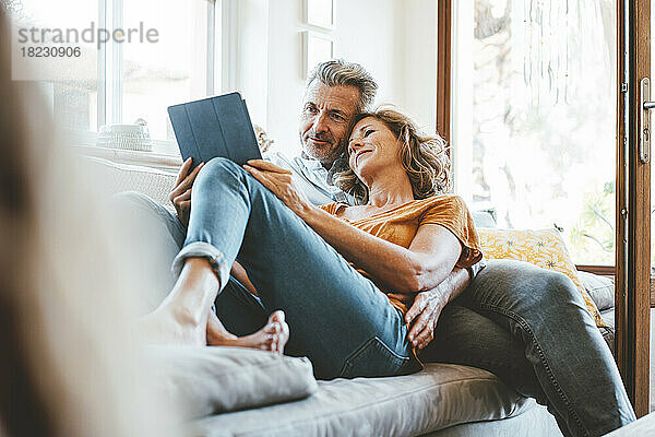 Liebevolles älteres Paar benutzt Tablet-Computer auf dem Sofa im Wohnzimmer