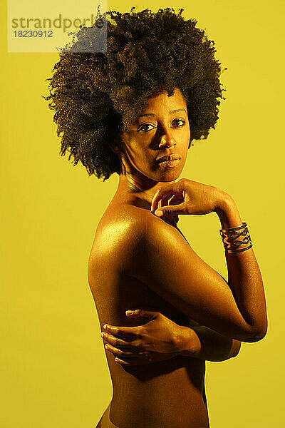 Selbstbewusste nackte Frau mit Afro-Frisur vor gelbem Hintergrund