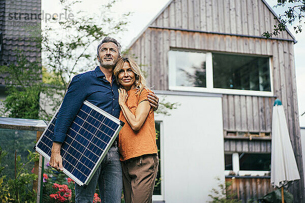 Älteres Paar steht mit Solarpanel vor dem Haus