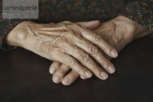 Ältere Frau mit faltigen Händen auf dem Tisch