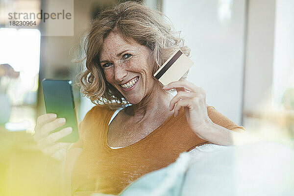Glückliche reife Frau sitzt mit Kreditkarte und Smartphone