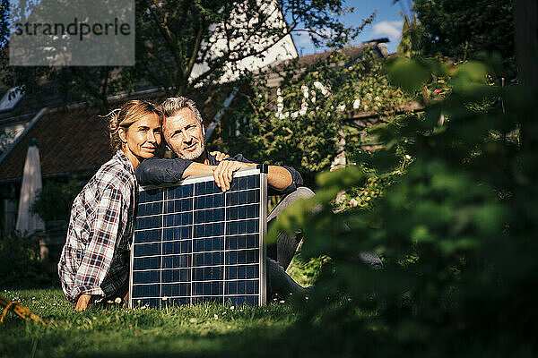 Lächelndes älteres Paar  das an einem sonnigen Tag mit Solarpanel im Hinterhof sitzt