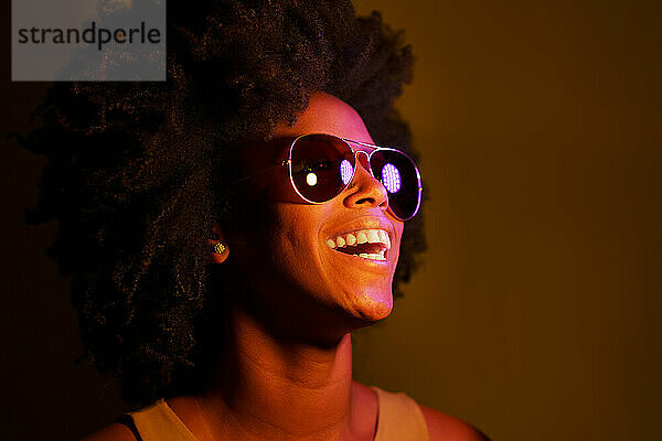 Frau mit Sonnenbrille lacht vor farbigem Hintergrund
