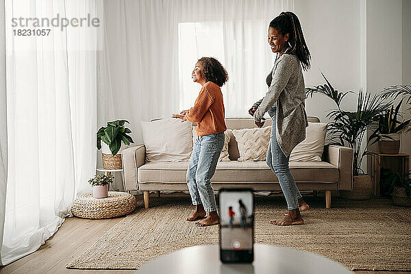 Glückliche Mutter und Tochter tanzen und nehmen zu Hause Videos per Smartphone auf