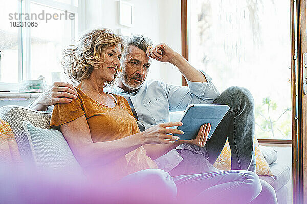 Lächelnde Frau teilt Tablet-Computer mit Mann auf Sofa zu Hause