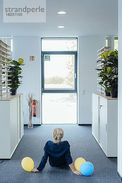 Businesswoman with balloons sitting on ground in office