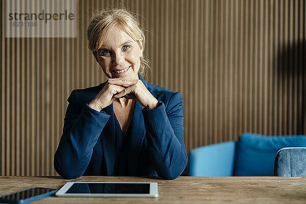 Glückliche Geschäftsfrau mit Tablet-PC und Smartphone am Schreibtisch
