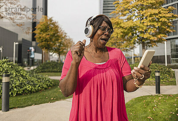 Fröhliche Frau mit Kopfhörern und Smartphone im Park